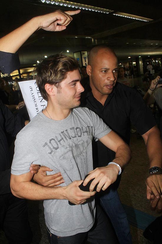 Segurança conduz o ator Zac Efron na chegada ao aeroporto internacional de Guarulhos, nesta terça-feira 