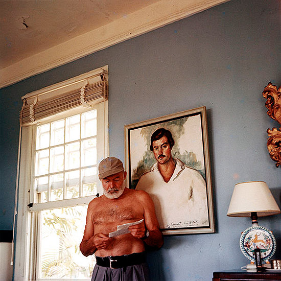 Ernest Hemingway em sua casa em Cuba, 1953, em frente a um retrato seu pintado por Waldo Pierce em 1929