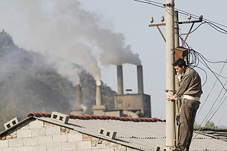 Homem trabalha com sistema elétrico na China, com chaminés ao fundo; Reino Unido anuncia verba para combater aquecimento até 2022