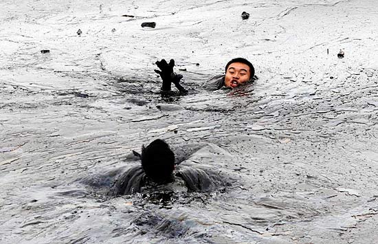 Bombeiro pula na água cheia de petróleo na costa da cidade de Dailinn, na China, para resgatar outro bombeiro