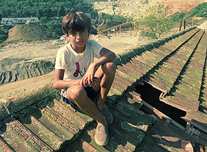 Marcelo, 10, e o buraco no telhado da escola atingida por pedra projetada da pedreira (ao fundo)
