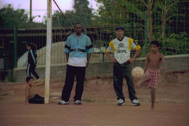 Garoto brinca com bola perto dos integrantes dos Racionais MC's, Ice Blue (à direita) e Mano Brown