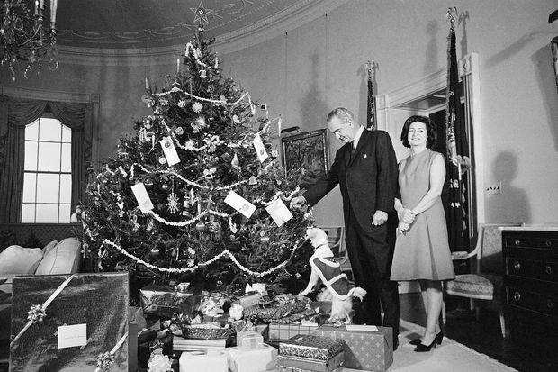 ORG XMIT: 373901_1.tif FILE - In this Dec. 24, 1967, file photo President Lyndon Johnson, Lady Bird Johnson, and Yuki, the White House pet, pose beside the family Christmas tree, a Norway spruce, in the Yellow Oval Room on the second floor of the White House in Washington. After President John F. Kennedy's assassination on Nov. 22, 1963, a month of mourning was declared. But on the evening of Dec. 22, Johnson lit the National Christmas Tree behind the White House, and the next morning the black mourning crepe that had been draped over White House doorways and chandeliers was replaced with holly, wreaths and mistletoe. Lady Bird Johnson later wrote, 