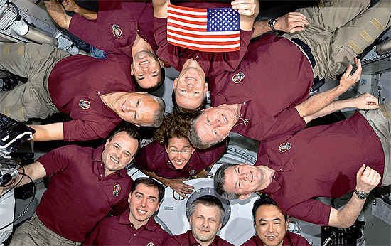 Astronautas na ISS posam com a primeira bandeira dos EUA a viajar em um ônibus espacial