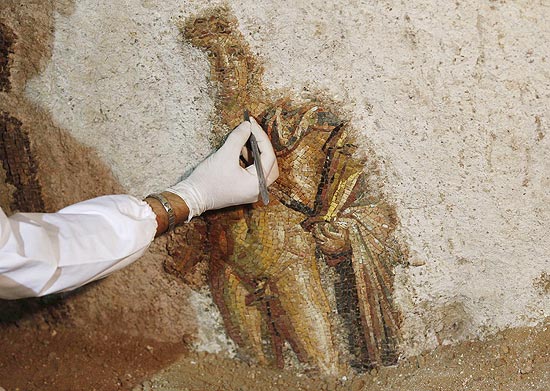 Funcionário limpa mural com o mosaico do deus grego Apolo; a peça foi encontrada no centro de Roma, na Itália