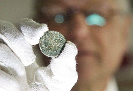 Homem exibe moeda que estava em assentamento romano, o último de cinco localizados pelos arqueólogos
