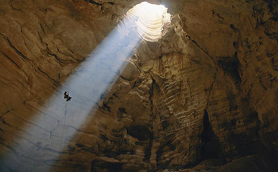 Um estudioso de cavernas desce às profundezas de Majlis al Jin, no Omã, iluminado por um raio de luz; veja fotos