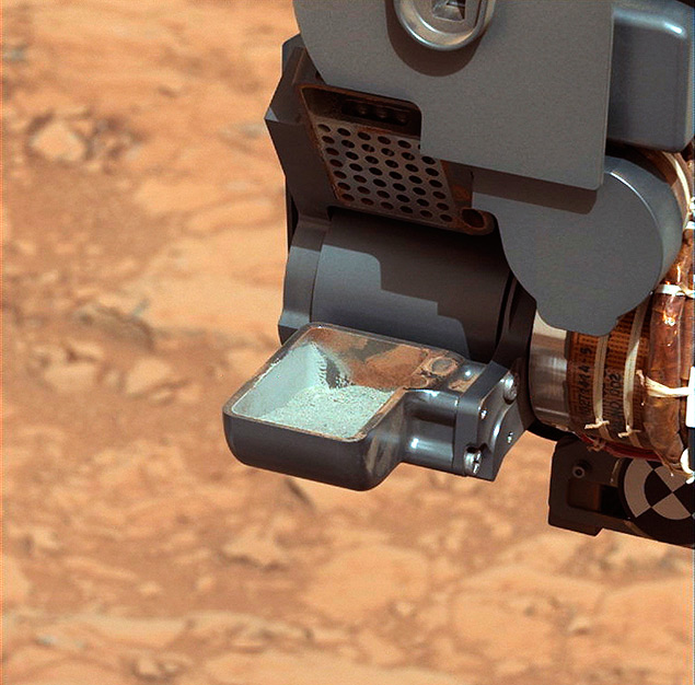 O jipe-rob Cusiosity mostra um p cinza, a primeira amostra de solo perfurado coletada em Marte, que permitiu a descoberta dos elementos qumicos bsicos para existncia de vida 