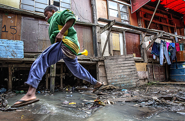 Morador de favela salta sobre esgoto a céu aberto