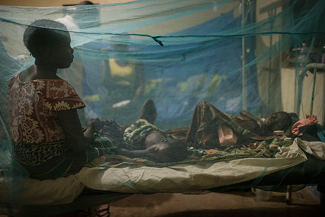 A woman sits under mosquito netting with her young children who are being treated for malaria, at a medical center in the the village of Kirando, Tanzania, July 19, 2014. The growing problem of mosquito-net fishing, which threatens stocks by scooping up too many small fish, is an unintended consequence of the successful distribution of nets to prevent malaria, one of the biggest and most celebrated public health campaigns in Africa. (Uriel Sinai/The New York Times)
