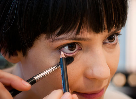 "Segurar" o olho com um pincel evita deixar marcas de dedos na maquiagem. Na foto, a maquiadora aplica o lápis bege na linha d'água