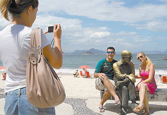 Turistas abraçam estátua de Carlos Drummond de Andrade e posam para foto; situação se repete várias vezes