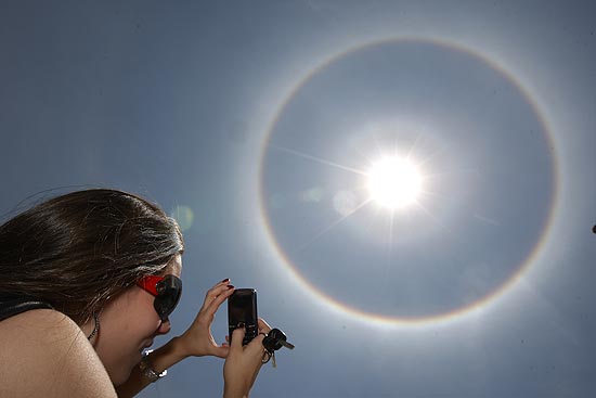 Mulher tira foto de halo solar em Brasília, resultado de ação de cristais de gelo; círculo pode ser também colorido