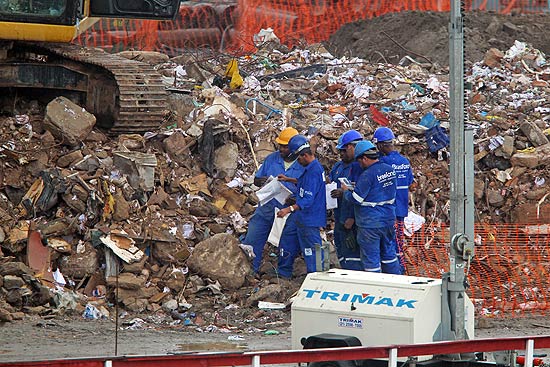 Operários observam papeis e álbum de fotos retirados dos escombros de três prédios no centro do Rio