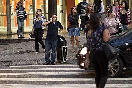 Pedestre falando no celular ao atravessar a rua Frei Caneca na esquina com a avenida Paulista