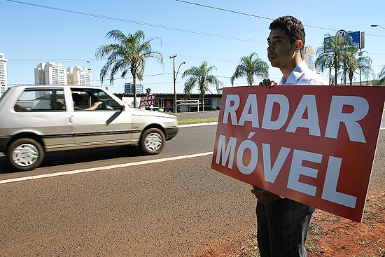 Marcos Antonio Alves, contratado por advogado, segura placa avisando de radar móvel em avenida de Ribeirão