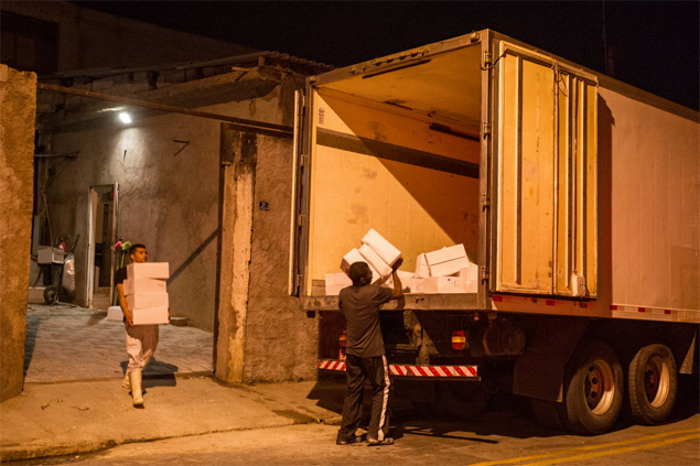Homens retiram carga roubada de 13 toneladas de bacalhau recuperada pela polícia em frigorífico em Guarulhos (Grande São Paulo)