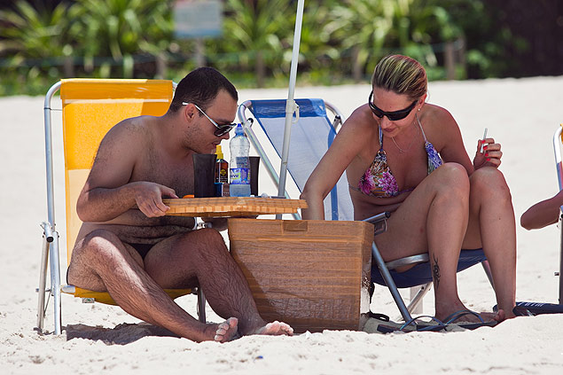 Casal com isopor com bebida na praia de Maresias; ambulante diz que vendas caíram
