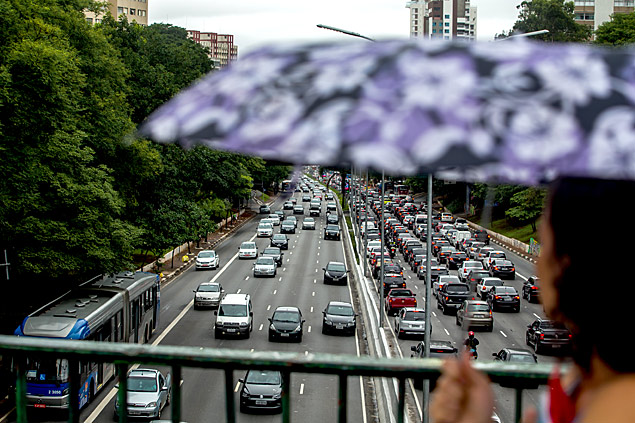 Mulher se protege da chuva na regio do Paraso; ao fundo congestionamento na avenida 23 de Maio