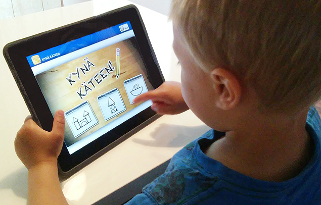 Criana finlandesa usa aplicativo para desenhar letras em aula; na tela do tablet, l-se, em finlands, 'pegue sua caneta'