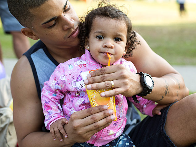 Bebê de 1 ano e 8 meses toma suco artificial em parque, acompanhada de seu pai