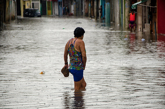Mulher caminha pela rua Agreste de Itabaina, na zona leste de So Paulo, durante alagamento
