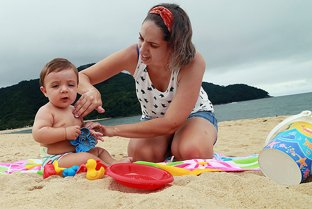 Camila, 32, passa protetor solar no filho Miguel, oito meses, na praia de Boiucanga (SP)