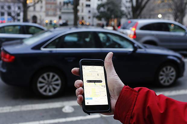 (FILES) This file photo taken on March 25, 2015 shows an UBER application viewed as cars drive by in Washington, DC. Uber has agreed to pay up to $100 million to settle two class action suits filed by drivers who said they were employees entitled to benefits, rather than independent contractors. The suits challenged a pillar of the business model of the pioneer of the so-called gig economy -- relying on workers with no set schedule and only a loose affiliation with the San Francisco-based company offering ridesharing services.Uber said in a statement April 21, 2016 it had agreed on a settlement with the plaintiffs. / AFP PHOTO / Andrew Caballero-Reynolds ORG XMIT: ACR01