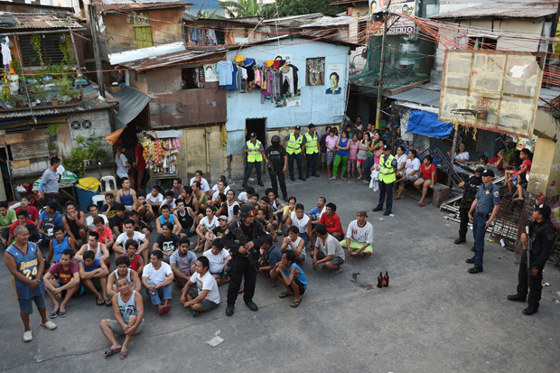 Dezenas de homens so reunidos em uma quadra de basquete em Manila e aguardam sentados no cho, vigiados por policiais, em operao contra as drogas.