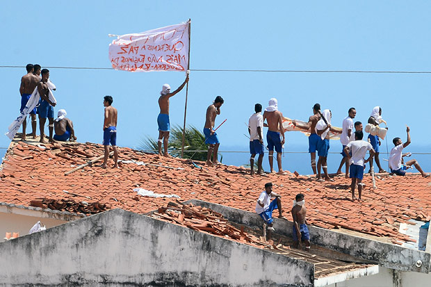 Inmates stand on the prison roof waving a flag with a message during a rebellion in Alcacuz Penitentiary Center near Natal, Rio Grande do Norte state, northeastern Brazil on January 16, 2017. The latest in a string of brutal prison massacres involving suspected gang members in Brazil has killed 26 inmates, most of whom were beheaded. The bloodbath erupted Saturday night in the overcrowded Alcacuz prison in the northeastern state of Rio Grande do Norte. Similar violence at other jails in Brazil left around 100 inmates dead in early January. / AFP PHOTO / ANDRESSA ANHOLETE