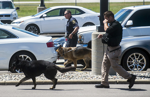 Police dogs search cars in a parking lot at Bishop International Airport, Wednesday morning, June 21, 2017, in Flint, Mich. Officials evacuated the airport Wednesday, where a witness said he saw an officer bleeding from his neck and a knife nearby on the ground. Authorities say the injured officer's condition is improving. (Jake May/The Flint Journal-MLive.com via AP) ORG XMIT: MIFLI208