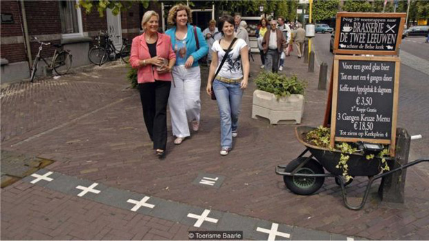 As fronteiras so marcadas por cruzes brancas nas caladas, indicando 'NL' de um lado e 'B' no outro | Foto: Toerisme Baarle 