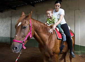 Samuel Sirqueira,5, com a fisioterapeuta Vanessa Brugiolo, faz exercícios em centro de equoterapia na Grande São Paulo