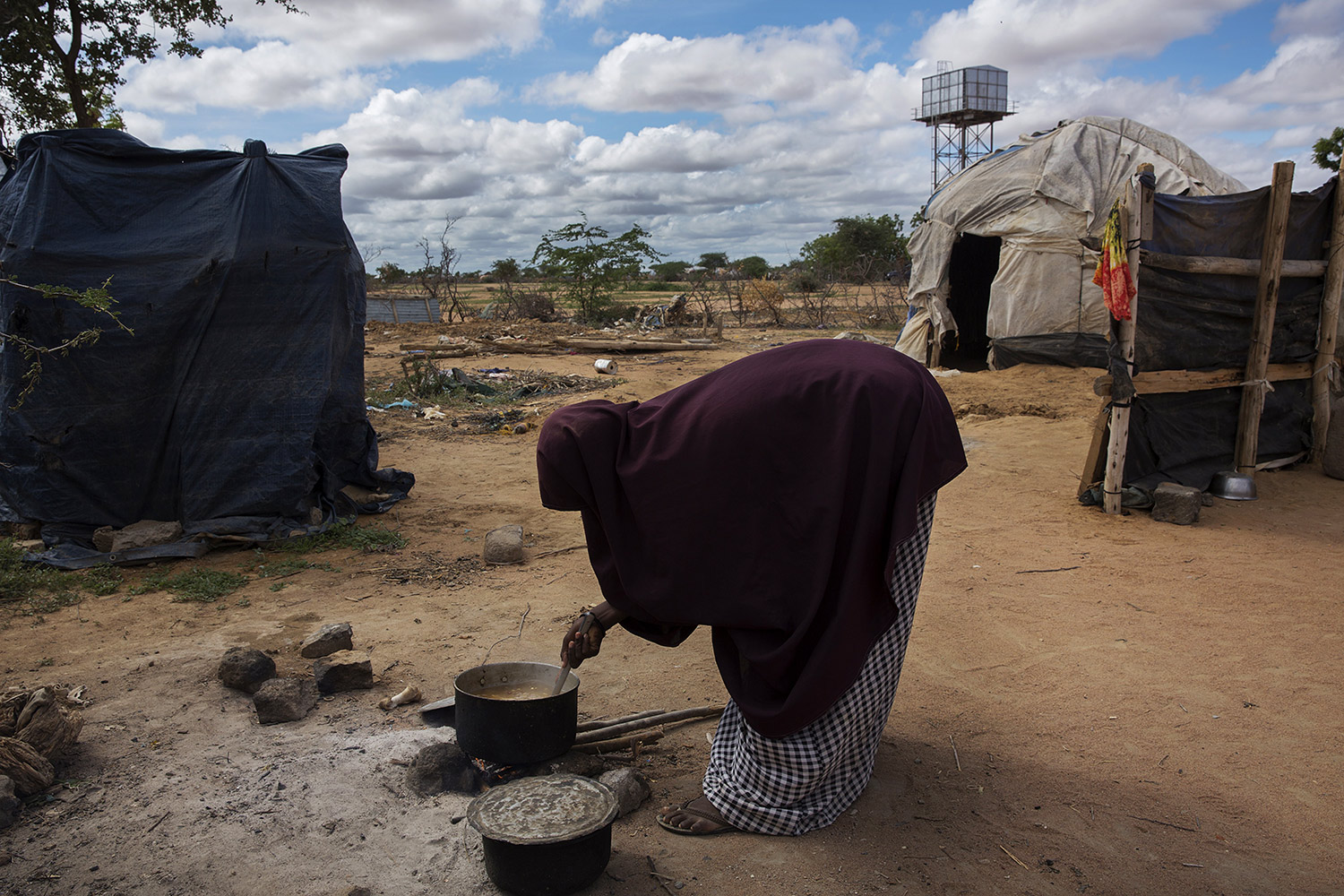 Abay, 20, filha de Noor Adow, recolhe folhas e cozinha em frente à sua tenda no campo de refugiados de Dadaab, no Quênia