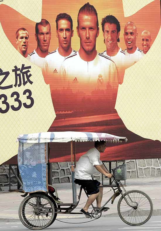 Homem pedala diante de cartaz com imagem de jogadores do Real Madrid, em Pequim, China, em 2005