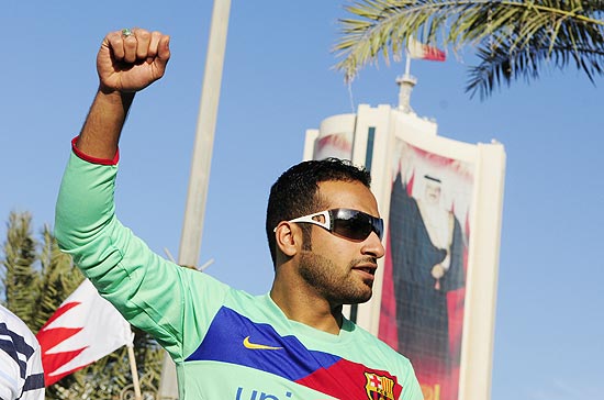 Manifestante xiita participa de marcha contra o governo, em Manama, tendo ao fundo um cartaz do rei