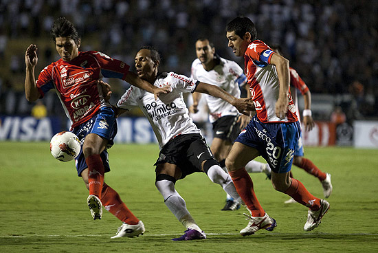 Liedson, do Corinthians, disputa a bola com os jogadores do Nacional Ramón Cáceres (esq.) e Denis Caniza
