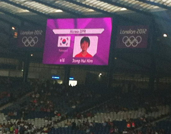 Imagem de jogadora da Coreia do Norte aparece ao lado da bandeira sul-coreana no telão do estádio em Glasgow, na Escócia