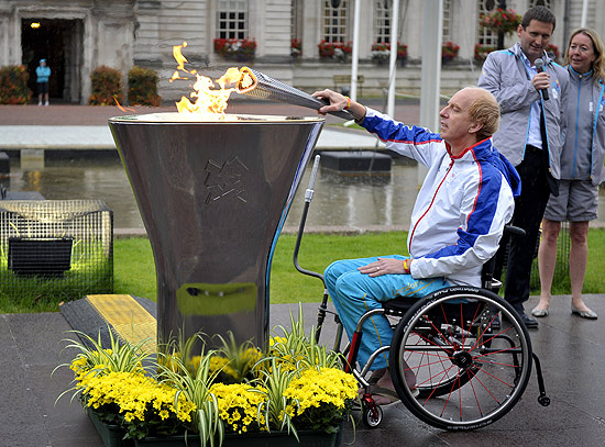 O atleta paraolímpico Simon Richardson acende a tocha olímpica no estádio de Cardiff