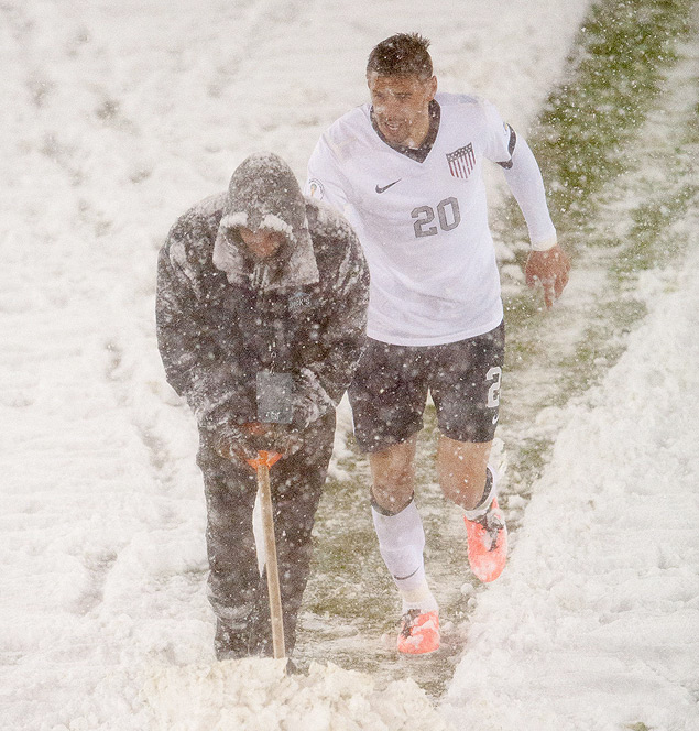 O jogador americano Geoff Cameron ajuda funcionrio a retirar neve do campo