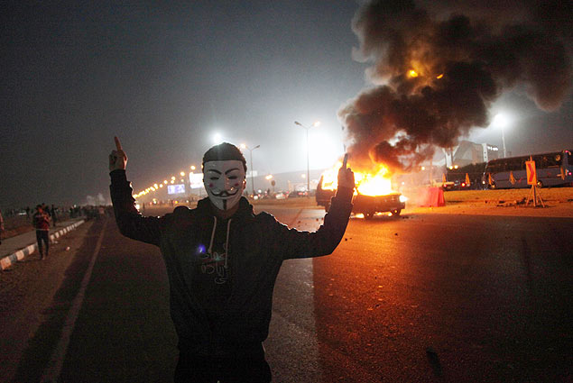 Homem mascarado posa ao lado de um carro incendiado, aps 22 mortes em partida de futebol no Cairo
