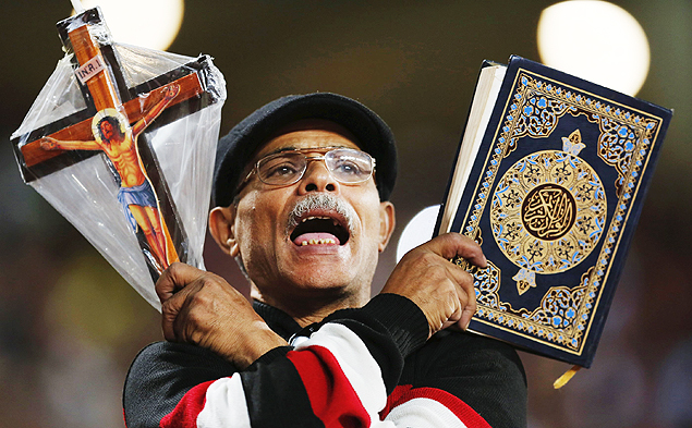 An Egyptian fan cheers and holds the Koran (R) and a cross before 2018 World Cup qualifying soccer match against Chad, at the Borg El Arab "Army Stadium" in the Mediterranean city of Alexandria, north of Cairo, Egypt, November 17, 2015.The match is the first in a long time that will played with spectators after receiving approval from security. REUTERS/Amr Abdallah Dalsh ORG XMIT: AMR121