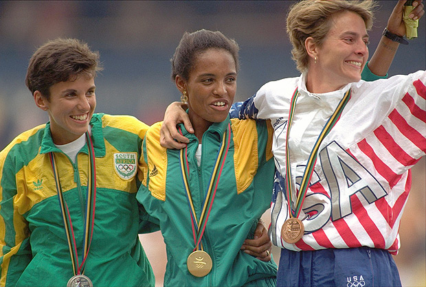 FILE - In this 1992, file photo, the medal winners, from left, South Africa's Elana Meyer, who won the silver, Ethiopia's Derartu Tulu, who won the gold, and United State's Lynn Jennings, who won the bronze, for the women's 10,000 meter race stand together during the awards ceremony at the Summer Olympics in Barcelona. Cold War boycotts aside, the games remain a symbol of global togetherness, even if an increasingly commercialized one. By putting religion and politics aside, the Olympics still can remind the world's people of their shared humanity, not their divisions. Once such moment was when white South African Meyer became her country's first post-apartheid individual medalist and ran over to plant a kiss on Tulu. (AP Photo/Deither Endlicher, File) ORG XMIT: OLY501