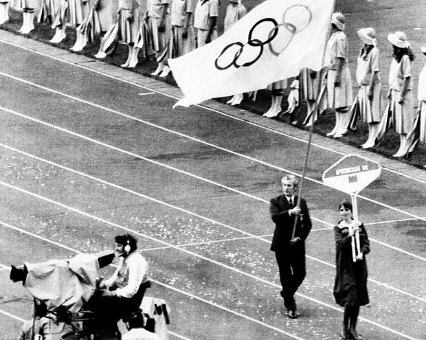 FILE - In this July 19, 1980 file photo a television cameraman points his camera in opposite direction as a Soviet woman carrying placard marked BOA for British Olympic Association is followed by Dick Palmer, secretary for British team, with Olympic flag during opening ceremony of Moscow Olympics. The IOC's ruling 15-member executive board will meet Sunday, July 24, 2016 via teleconference to weigh the unprecedented step of excluding Russia as a whole from the 2016 Rio Olympic Games because of systematic, state-sponsored cheating. (AP Photo) ORG XMIT: FOS112