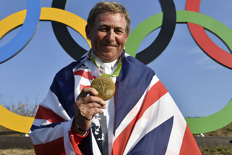 Britain's Nick Skelton celebrates with his gold medal in front of the Olympic rings after the individual equestrian show jumping event during the Rio 2016 Olympic Games in Rio de Janeiro on August 19, 2016. / AFP PHOTO / John MACDOUGALL