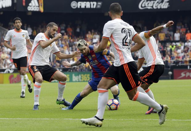 FC Barcelona's Lionel Messi, center, duels for the ball during the Spanish La Liga soccer match between Valencia and FC Barcelona at the Mestalla stadium in Valencia, Spain