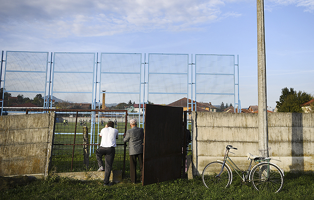 Two men watch through a wall as FK Trepca, a team from Mitrovica, Kosovo, that crossed the border to play a Serbian fourth-tier soccer match, in Mrcajevci, Serbia, Oct. 2, 2016. Mitrovica was once one of the richest, most vibrant places in Yugoslavia, its mixed-ethnicity soccer club a point of pride. Now Trepka is just one more sore point in a bitterly divided city. (James Hill/The New York Times)  NO SALES  - XNYT45