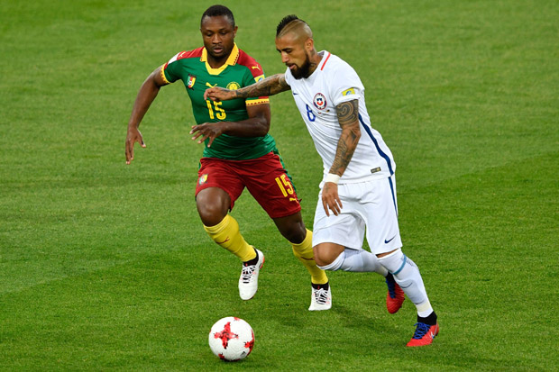 O camaronês Sebastien Siani (esq.) disputa bola com o chileno Arturo Vidal em jogo no domingo (18)