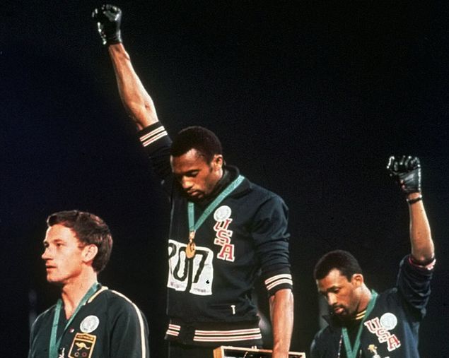FILE - In this Oct. 16, 1968, file photo, extending gloved hands skyward in racial protest, U.S. athletes Tommie Smith, center, and John Carlos stare downward during the playing of 