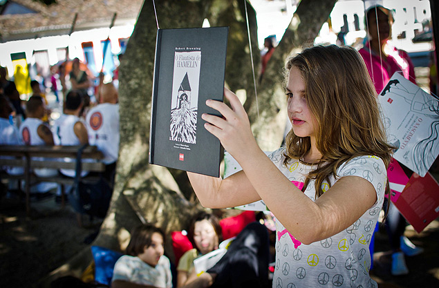 Menina observa livro pendurado em rvore na Flipinha